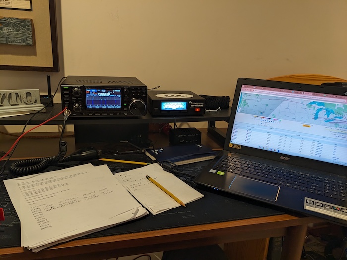 Photo of W1YTQ's radio station with a map showing propagation on a laptop and a half filled out paper log sheet with the RandomGram random groups on it