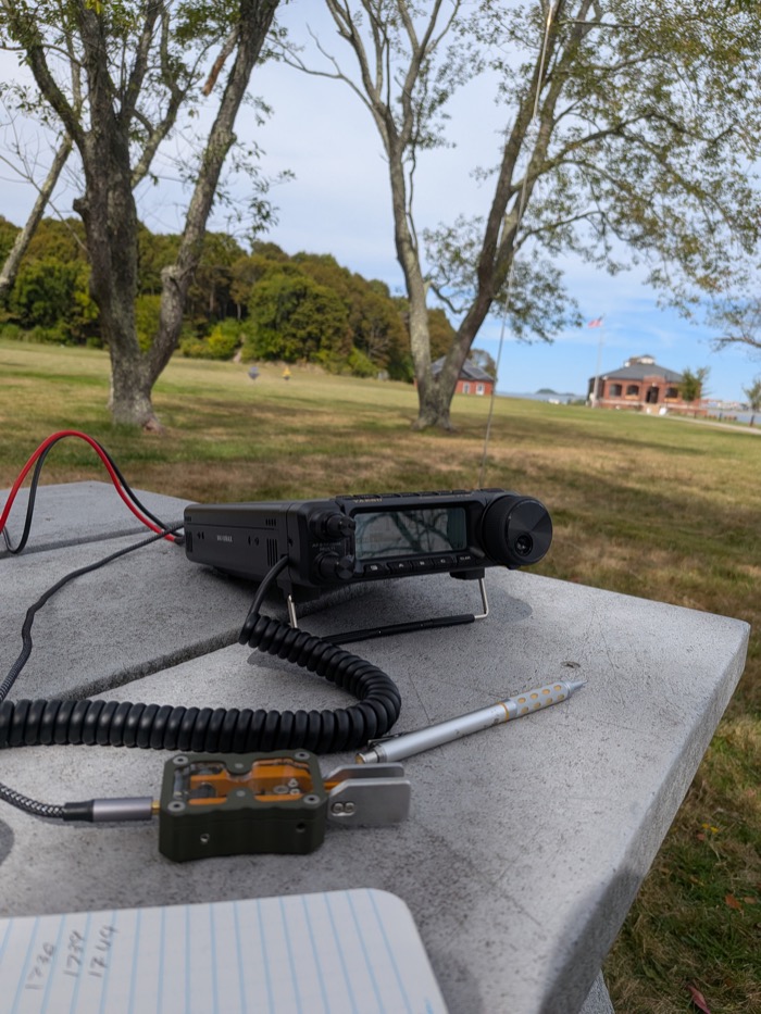 My Yaesu FT-891 and quarter-wave vertical set up on a picnic table at Peddocks Island, Fort Andrews in the background