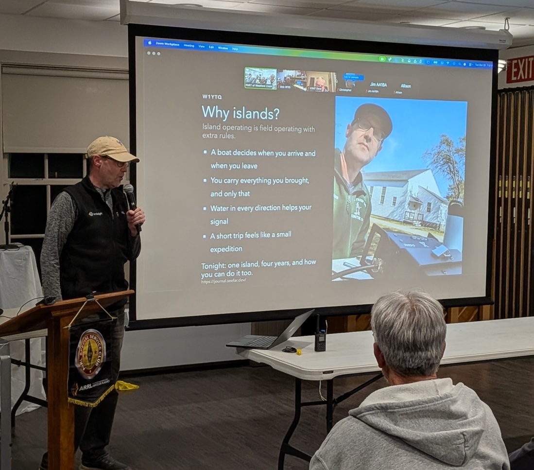 Chris Farnham (W1YTQ) at a podium with a microphone, presenting a slide titled "Why islands?" on a projector screen with the Zoom attendees along the top