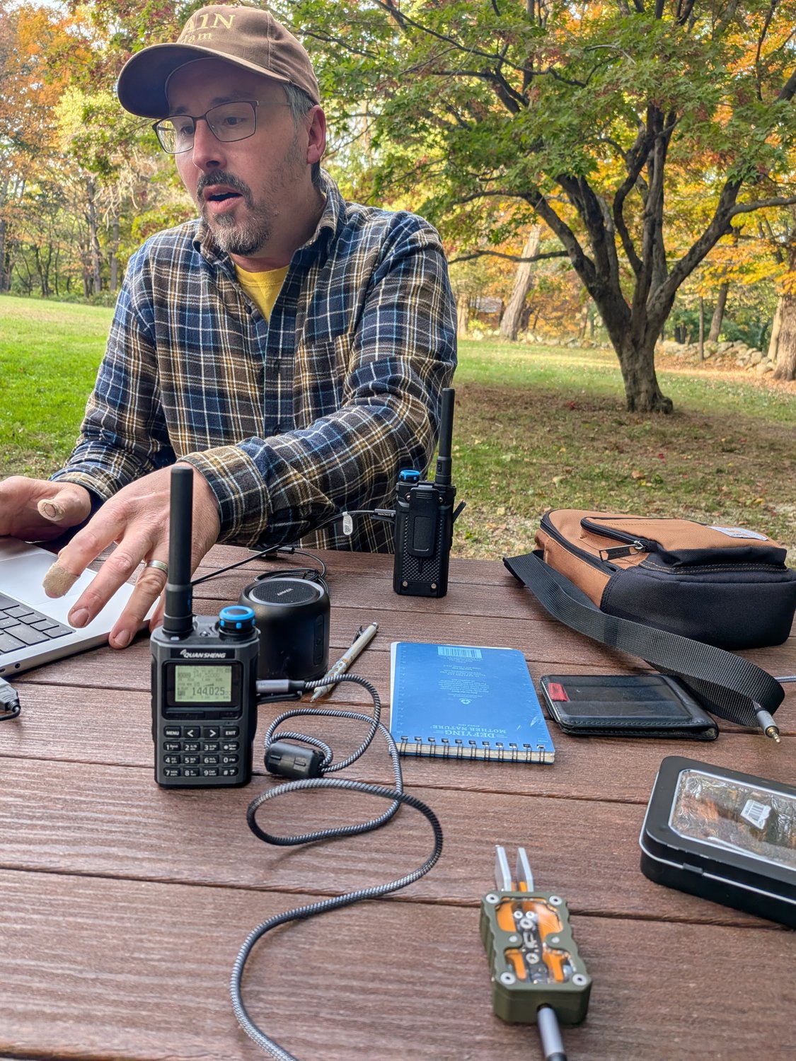 Adam (AA1N) at a picnic table at Minute Man National Historical Park with a laptop, two handheld radios and a notebook