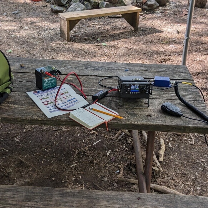 Xeigu G90 radio, log book and battery on a picnic table